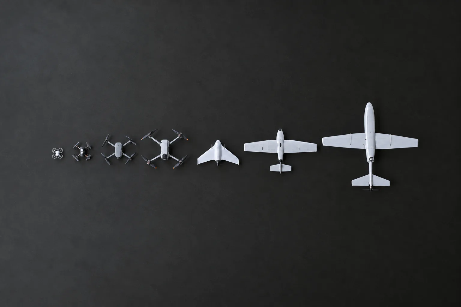 A row of aircraft arranged from smallest to largest on a clean dark floor, top down